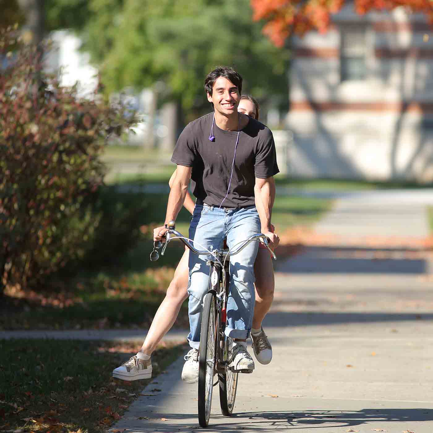 Two students share a bike on one of the campus paths